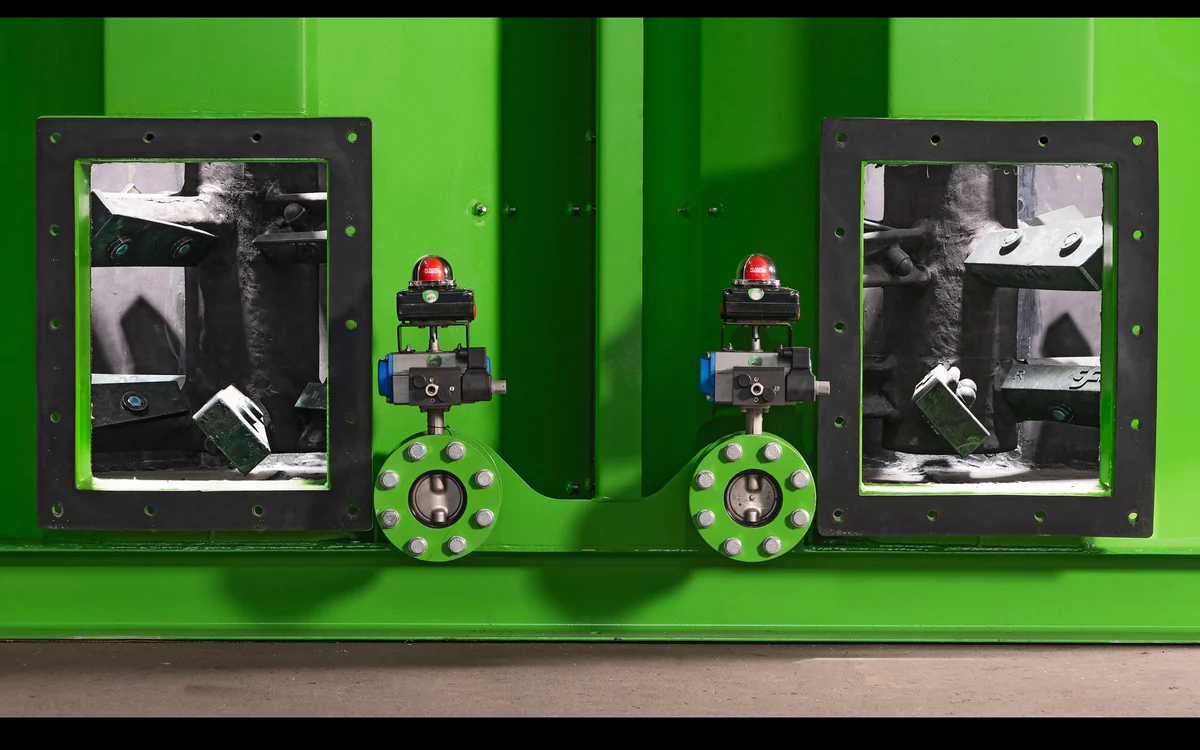 Close-up of the side of a green Atropure attrition scrubber, two tempered glass inspection windows showing the staggered impeller blades inside each cell, with the pneumatic butterfly valves and their red closed-position indicators between them