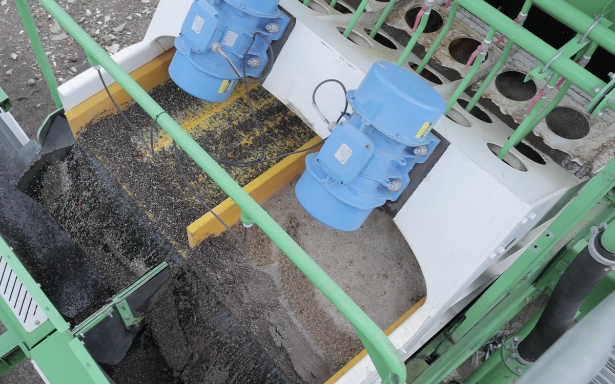 Looking down onto a Centriscreen deck in production, twin blue exciter motors on the screen box, washed sand and dark fines running off two sides of the deck and the bank of cyclones alongside
