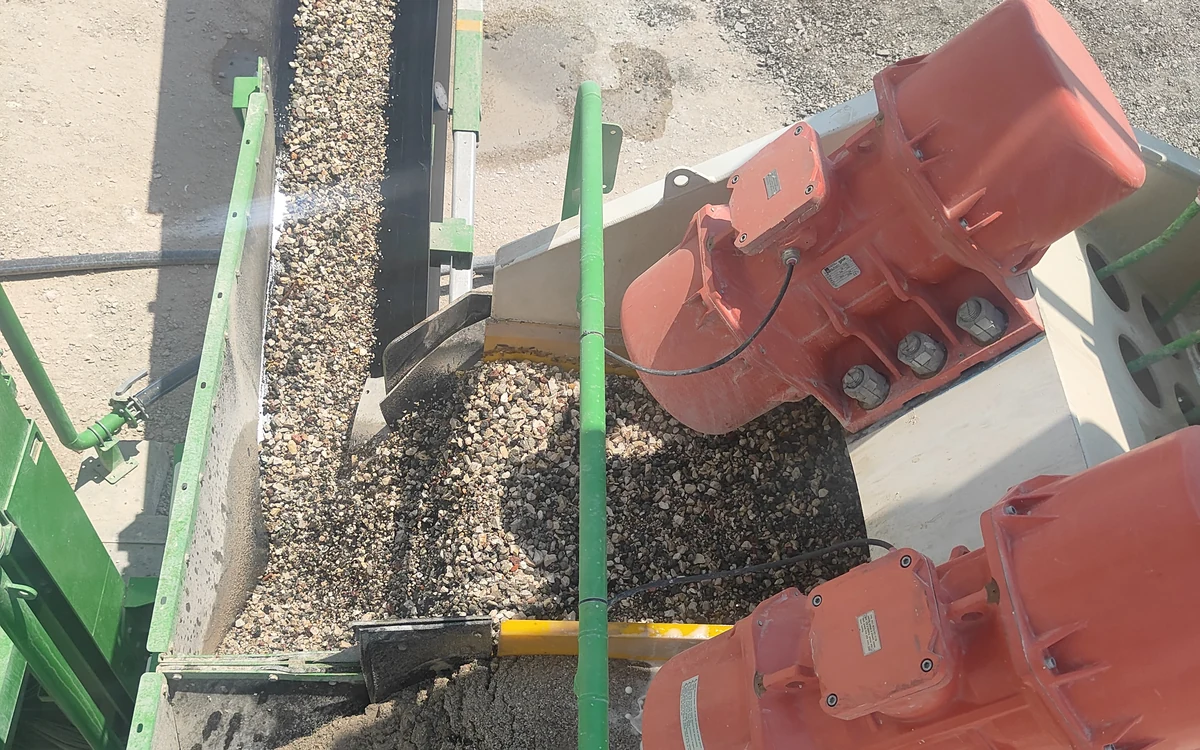 A Centriscreen discharging two products at once, washed gravel onto one conveyor and damp sand onto another below it, with the red twin exciters mounted on the screen box alongside