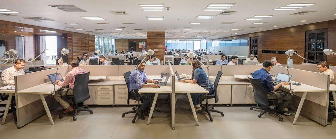 CFlo's Kolkata head office, an open floor of desks with engineers working at laptops under task lamps, glazing along the far wall looking out to greenery