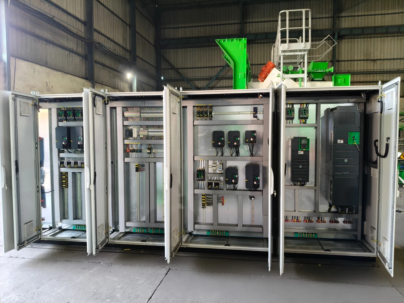 The full line-up of CFlo PLC control panels in the works, four cubicles with every door open, showing the drives, breakers, terminal rails and numbered wiring inside each, with a green plant module standing behind them
