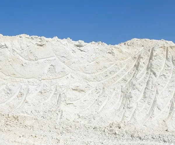 A long white stockpile of processed kaolin with loader tracks across its face
