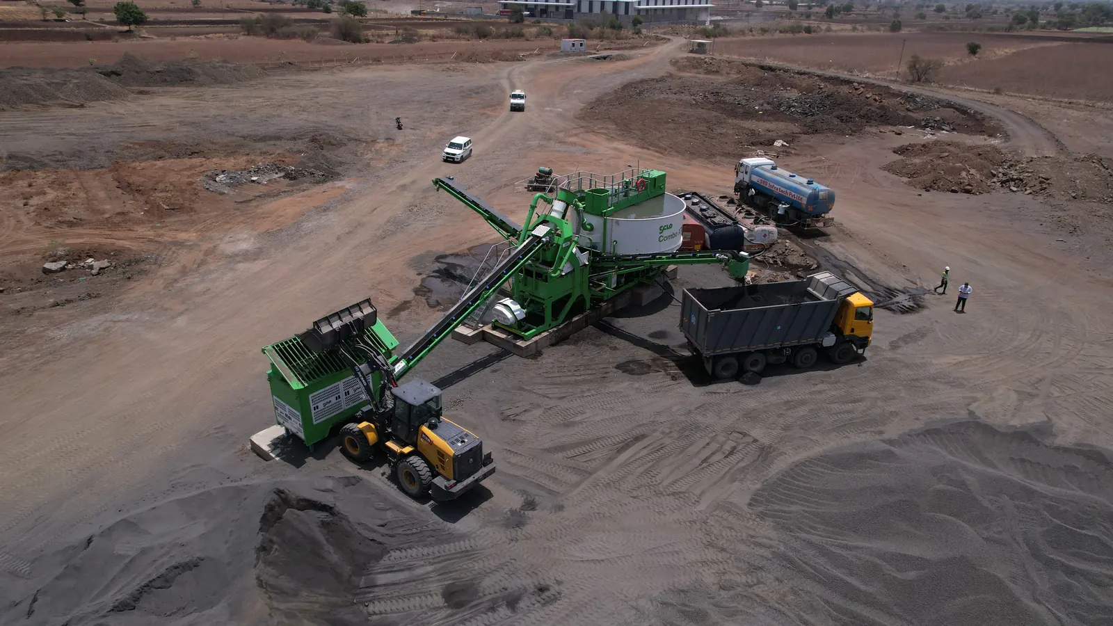 Aerial view of a CFlo Combo X50 on a sand site, a wheel loader charging the feed hopper while the product conveyor loads a waiting tipper truck