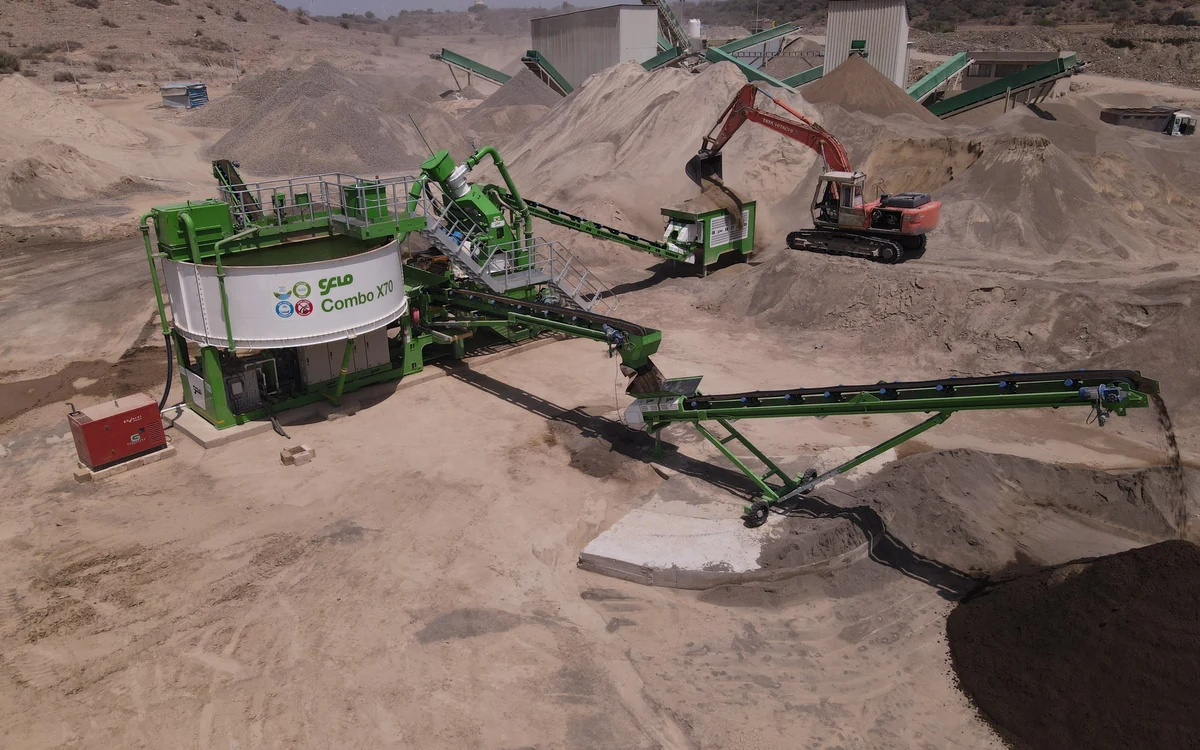 A CFlo Combo X70 working in a quarry, its white thickener tank beside the washing module, a tracked excavator feeding the hopper and product conveyors running out to stockpiles of washed sand and dark fines