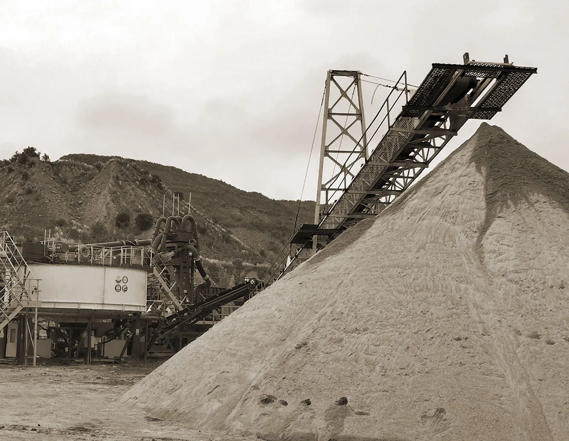 A radial conveyor discharging onto a tall conical sand stockpile at a quarry