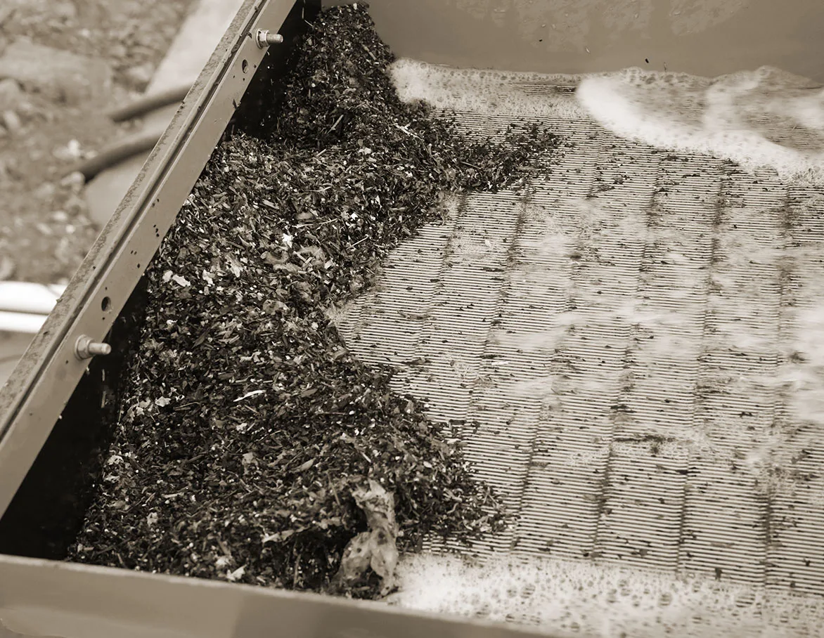 Dark wet aggregate travelling across a vibrating screen deck under water spray
