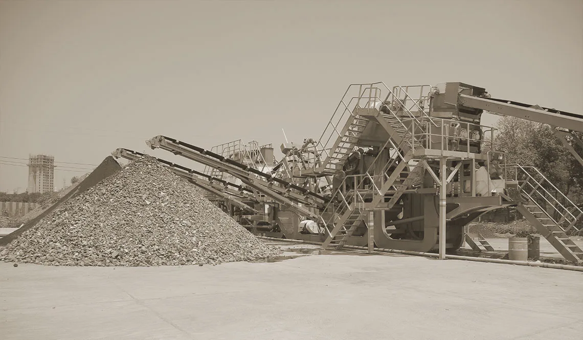 A conveyor discharging a stockpile of grey aggregate beside plant steelwork
