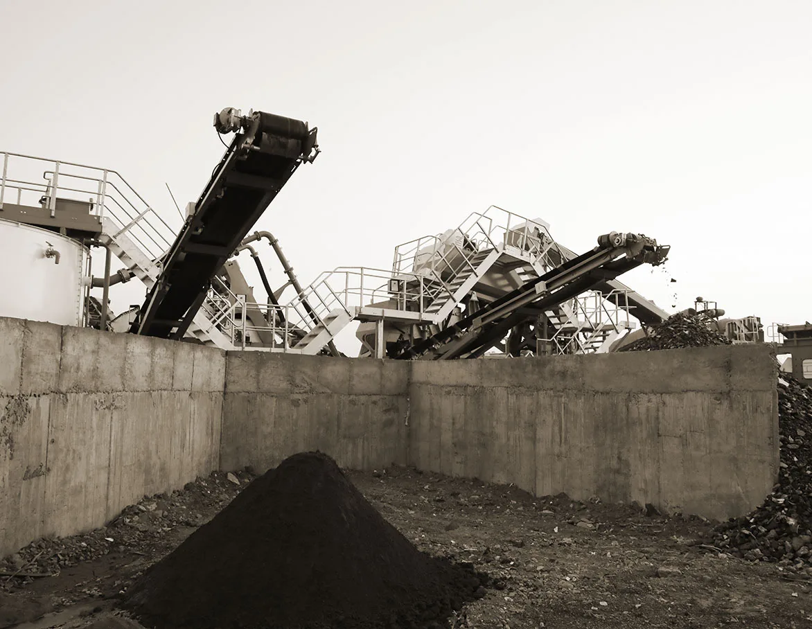A washing plant behind a concrete retaining wall with a black stockpile of processed material