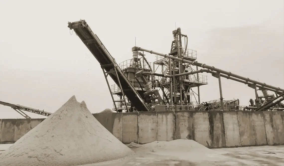 A washing plant on a concrete pad discharging a tall pale sand stockpile