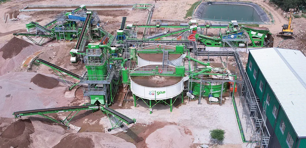 Aerial view of a green CFlo plant among pink-red ore stockpiles, with settling ponds and a site cabin