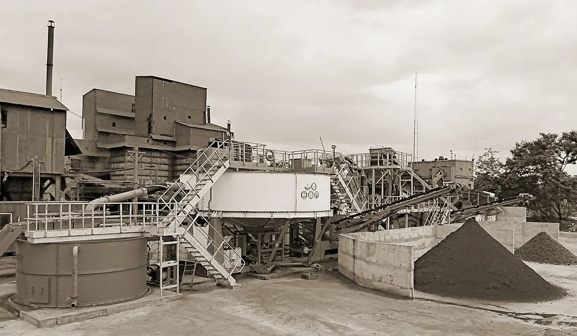 An industrial plant building with a circular thickener tank and conveyors in the foreground