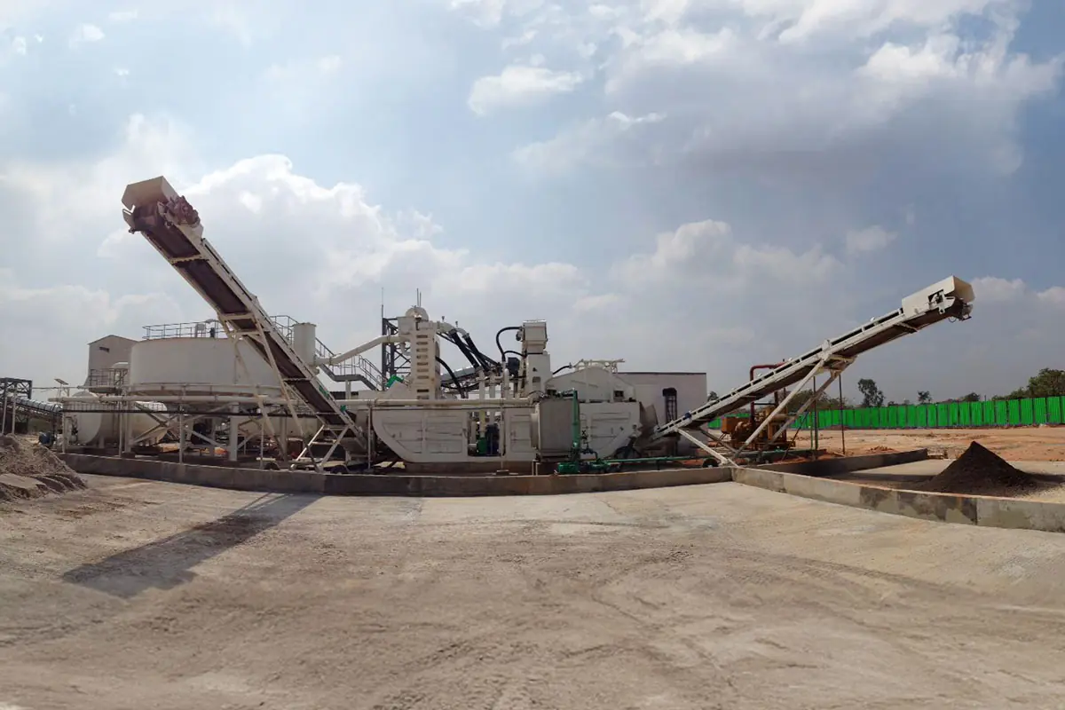 A long low plant with a raised radial conveyor on a flat sandy site under cloud