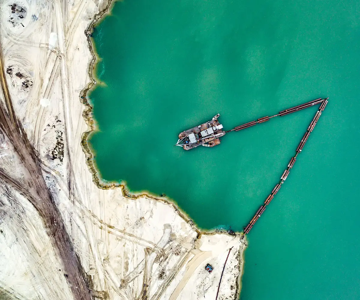 Aerial view of a dredger working on a turquoise reservoir, its floating pipeline reaching the shore