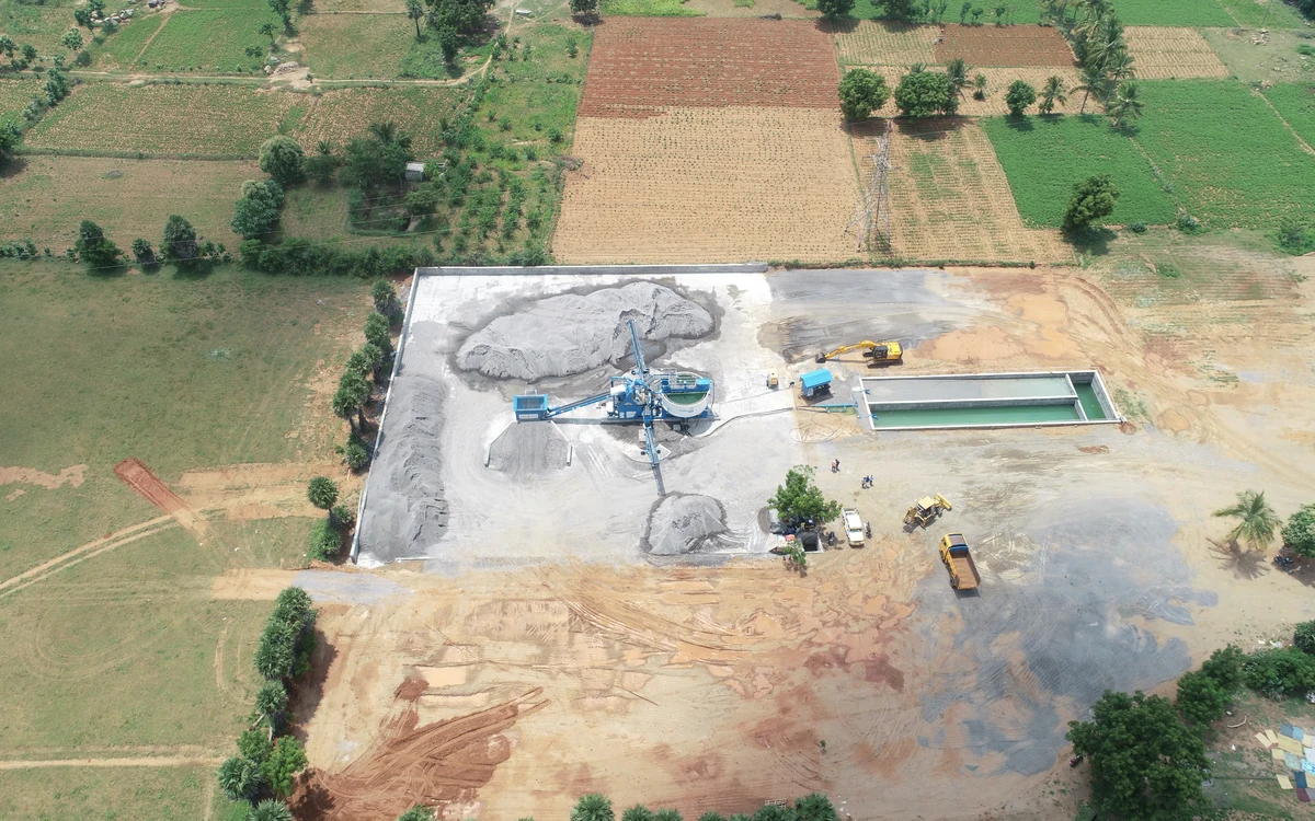 Aerial view of a wash plant on a walled concrete pad, sludge bays of drying cake beside the plant and a lined water recovery pond alongside, with farmland all around