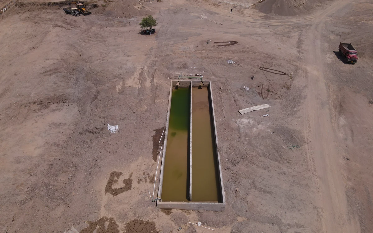 Aerial view of twin Easysettle bays on an arid site, one holding green clarified water and the other the brown sludge still releasing it, with the wash plant and stockpiles beyond