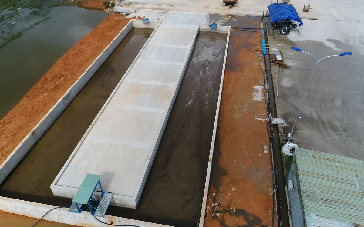 Looking down into a pair of Easysettle bays divided by a concrete wall, treated sludge settling dark on one side while clear separated water stands on the other, ready to be pumped back to the wash plant