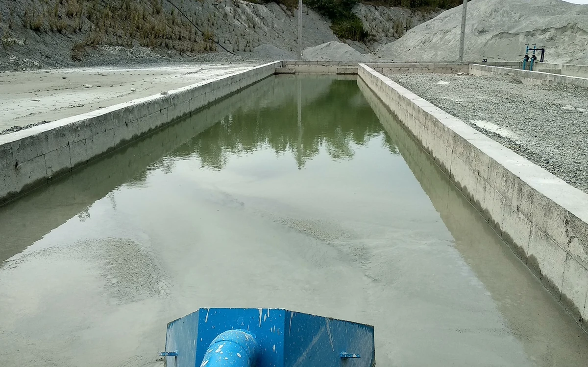 Treated slurry discharging from a blue inlet pipe into a concrete Easysettle bay, the solids rigidifying at the inlet end while clear separated water stands across the rest of the bay