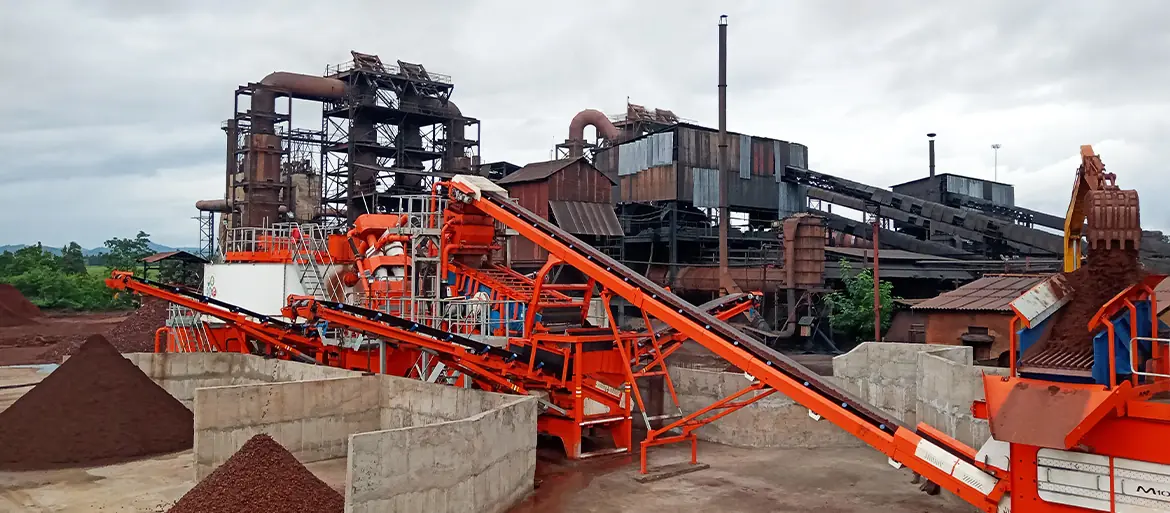An orange-painted ore processing plant with conveyors and red-brown stockpiles