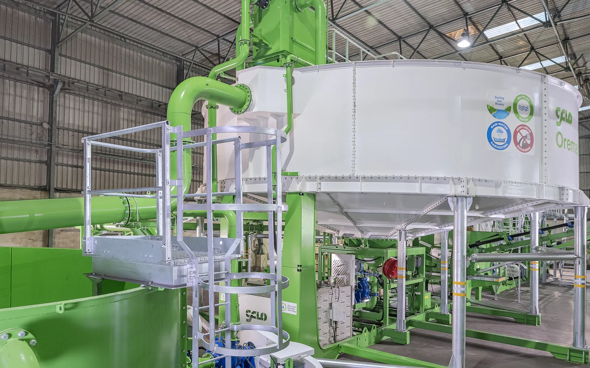 Hydromax H600 thickener in the works, the white bolted sectional tank raised on galvanised legs above its conical sludge outlet, with the green feed pipework and de-aeration chamber rising at the left and the sludge pumping station beneath