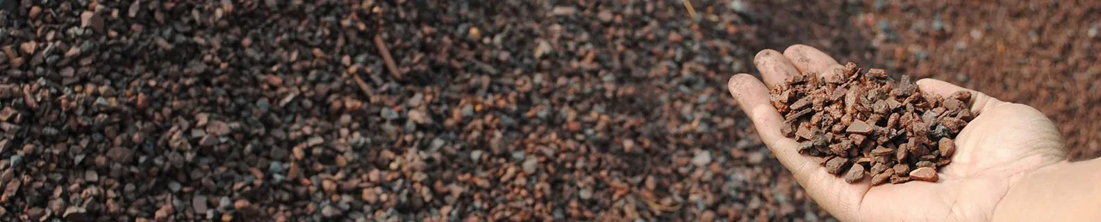 A hand holding fine red-brown iron ore fines above a bed of the same material