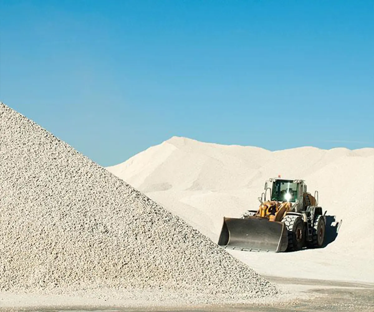 A wheel loader at the foot of a very large pale limestone stockpile