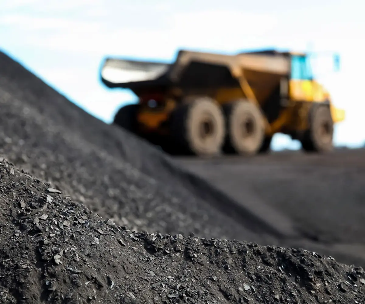 A haul truck on the crest of a dark manganese ore stockpile
