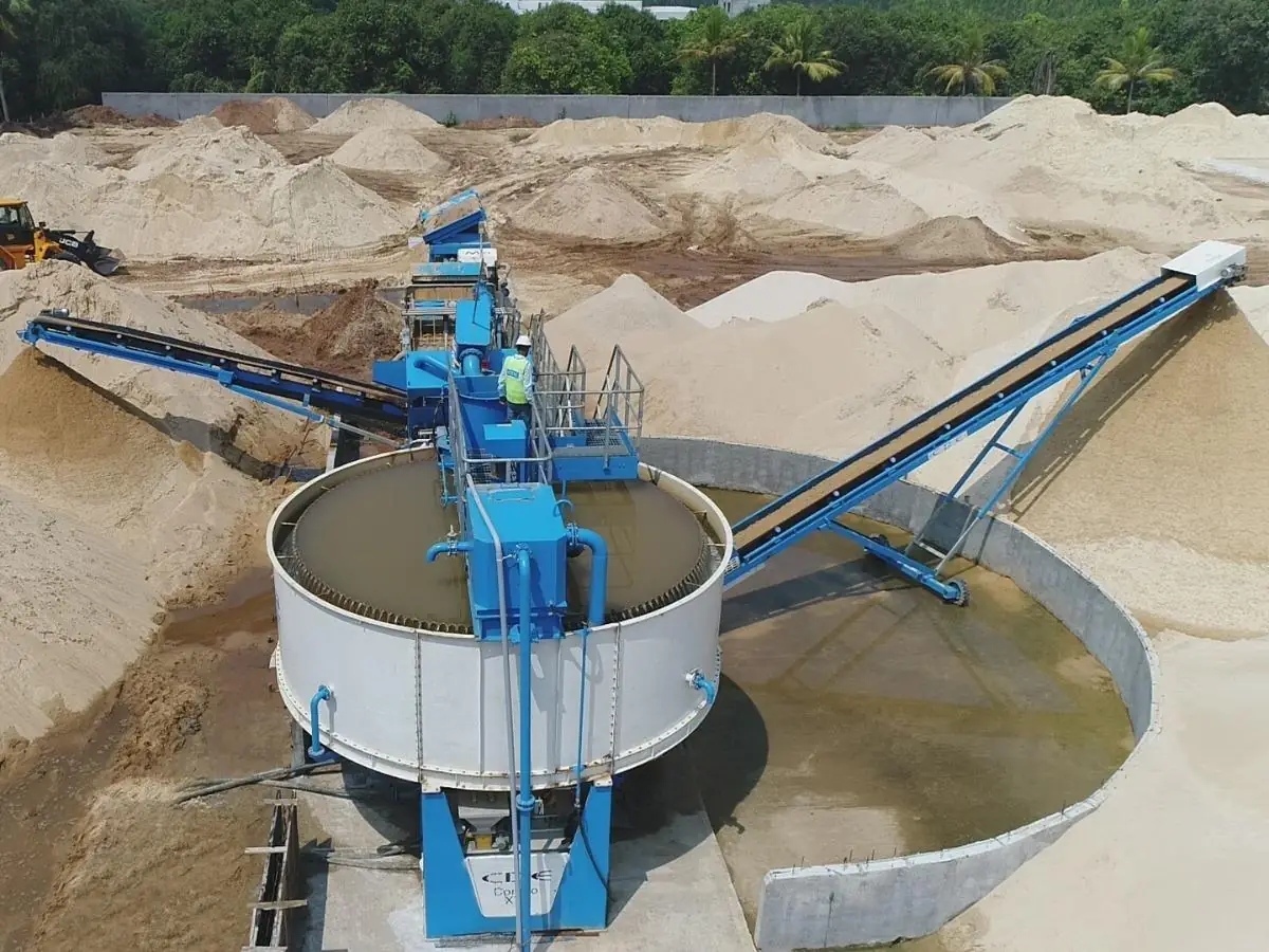 A blue washing plant with a circular tank and inclined conveyor among pale sand stockpiles