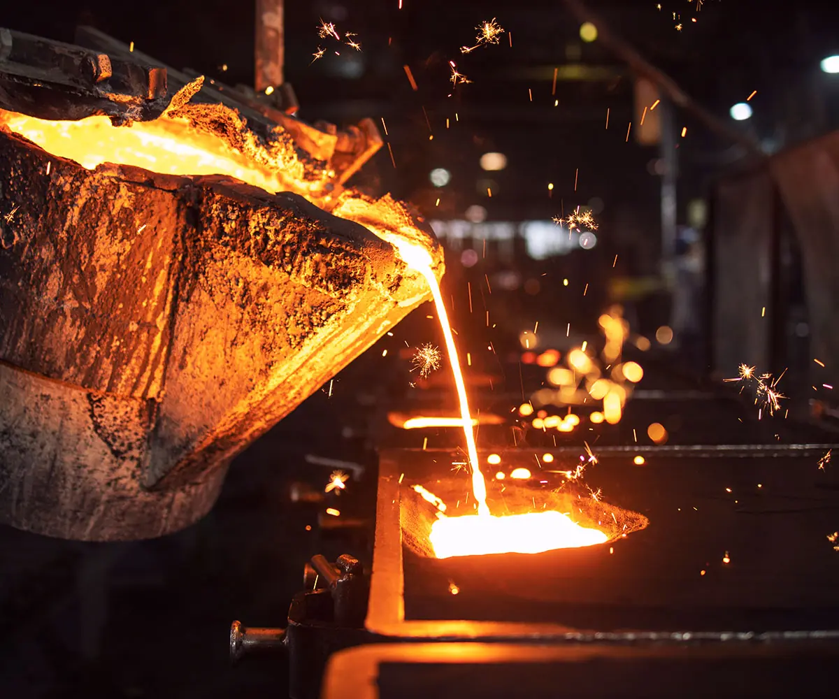 Molten metal being poured from a ladle, sparks rising, in a foundry