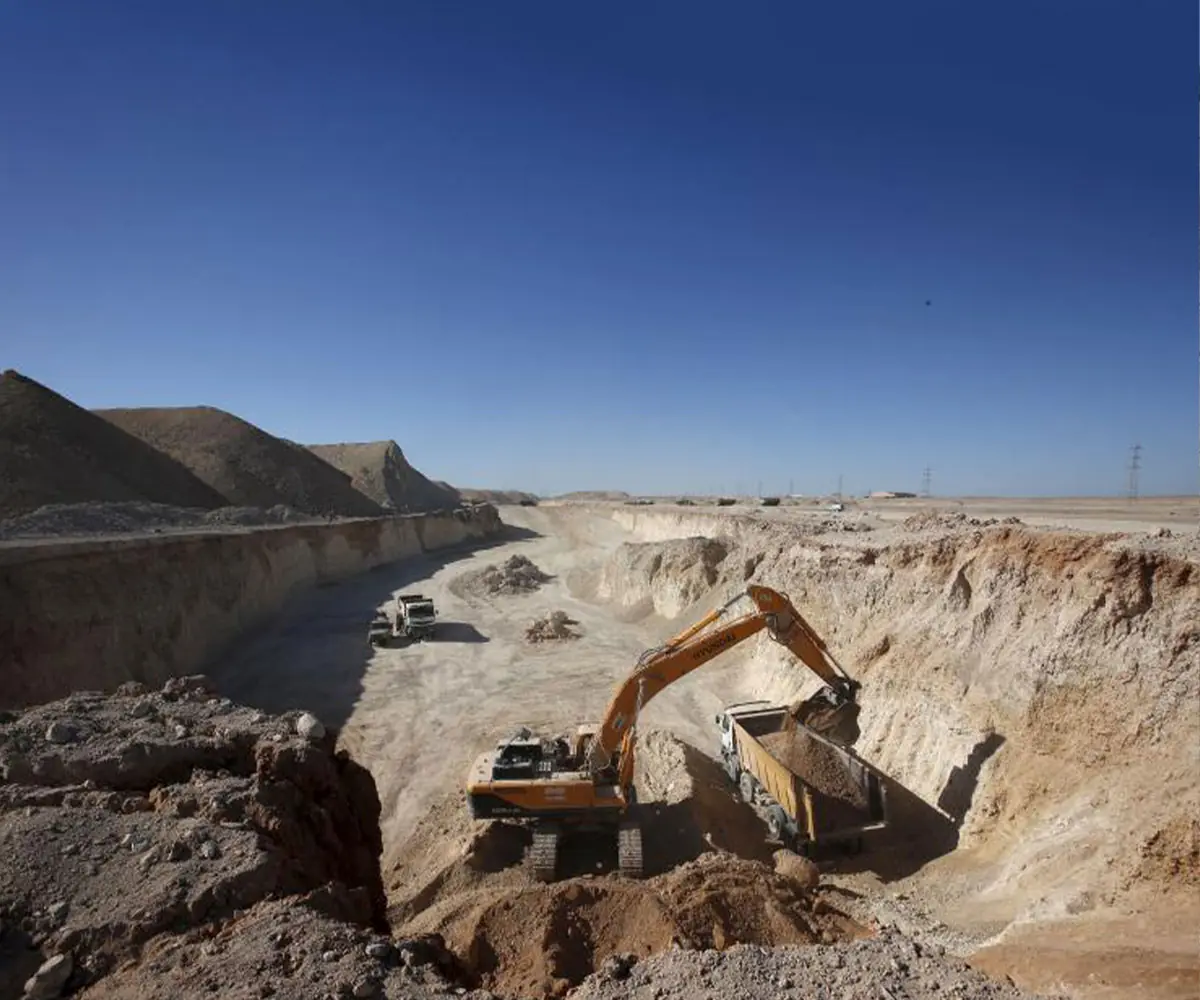 An excavator loading a truck in a wide open pit with water at its floor