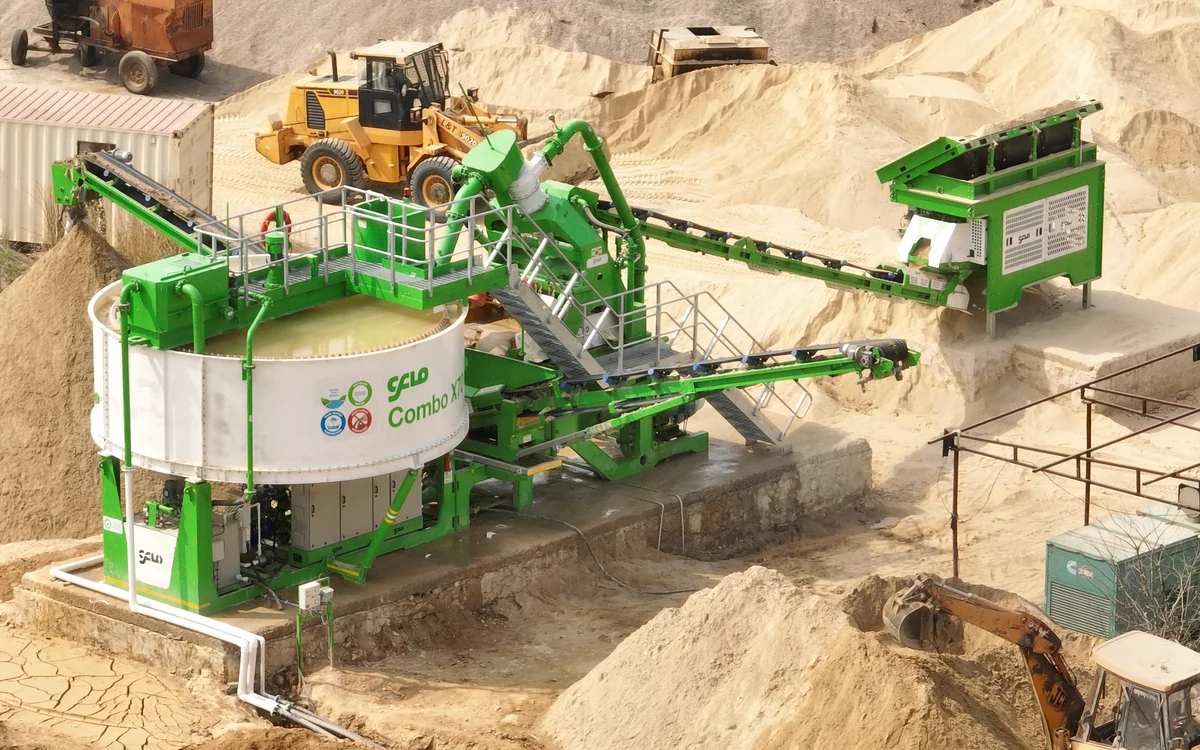 CFlo Combo X70 working in a sand pit, its white thickener tank full of clarified water beside the washing module, with a wheel loader feeding the hopper and worked sand faces rising behind