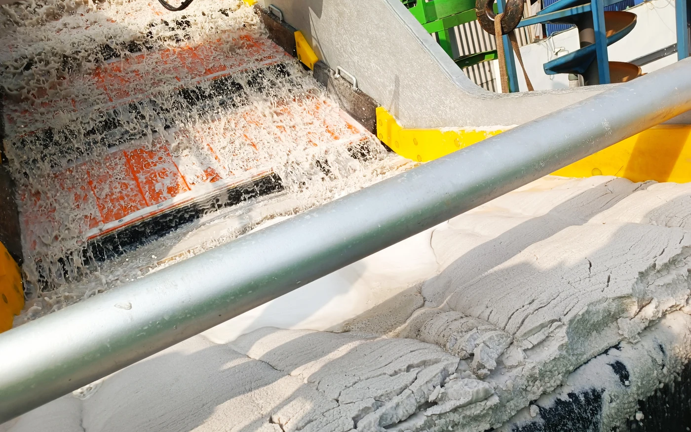 Looking down a Screenmax FS86 deck in production: slurry sheeting over the orange polyurethane panels with the black repulping zones between the steps, and a stockpile of washed white sand discharged in the foreground