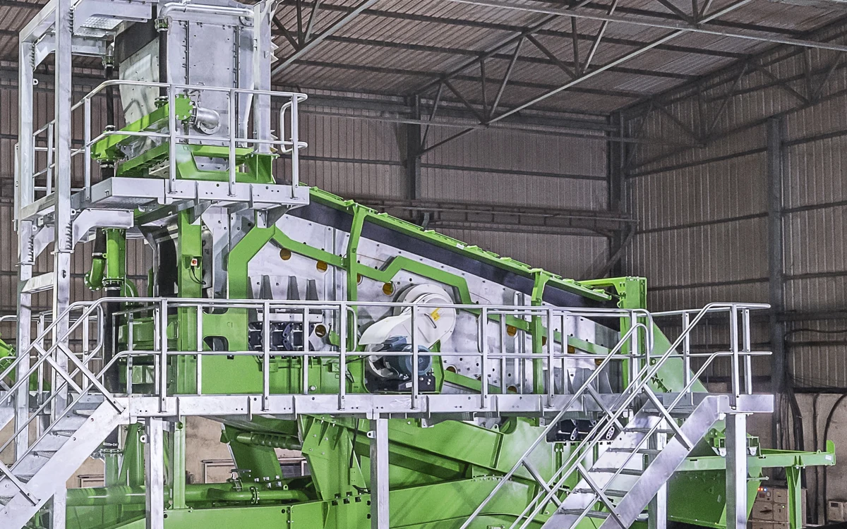 Screenmax G series circular motion rinsing screen in the works, the inclined screen box on its green frame with the drive and flywheel on the side, the feed chute above and galvanised walkways and stairs around it