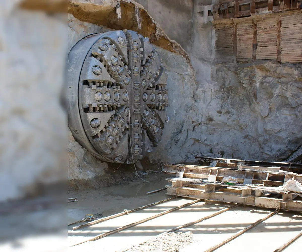 The cutting head of a tunnel boring machine at the face, with track and timbers in the foreground